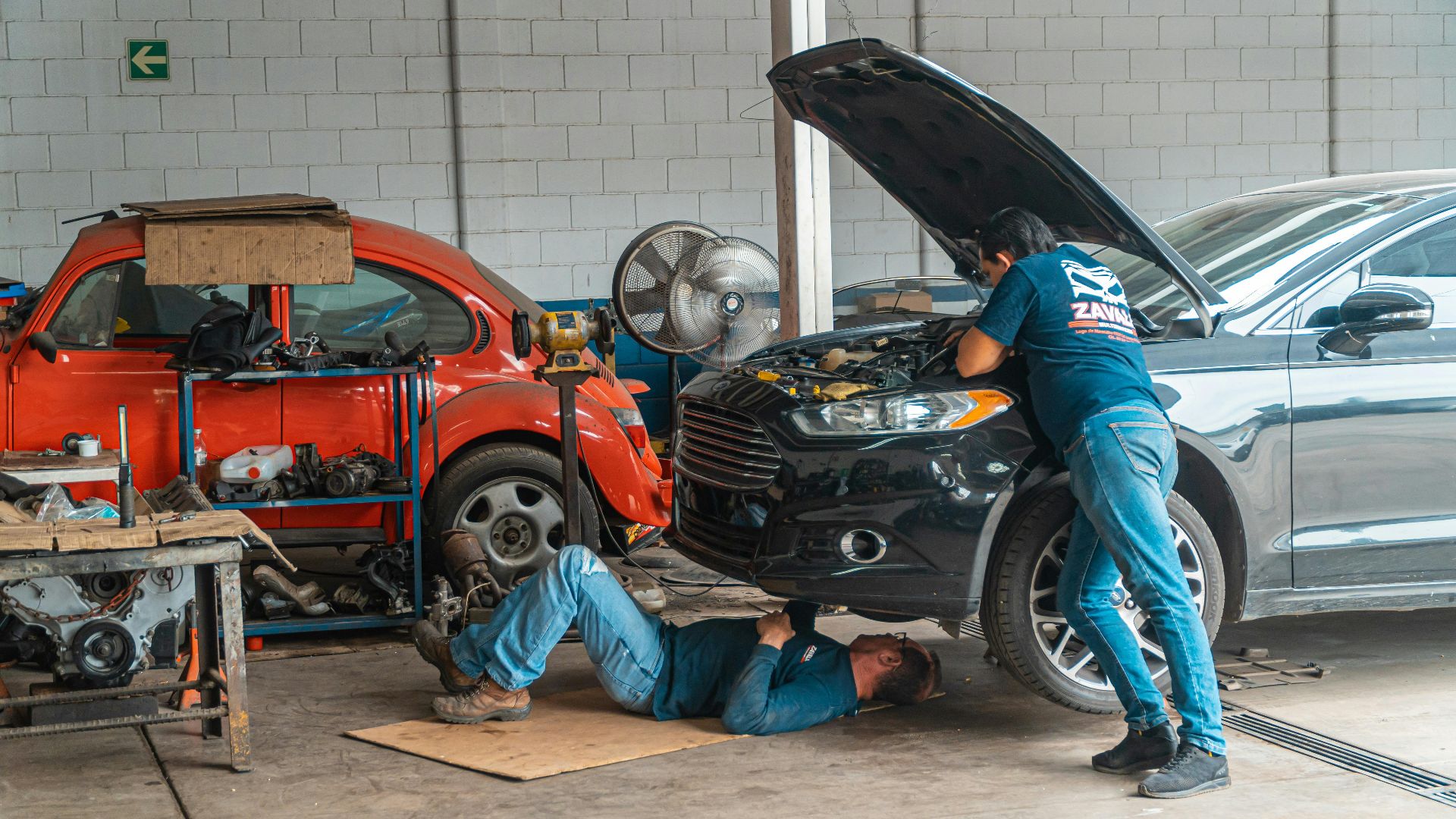 Mechanics working in an automotive workshop, repairing cars and performing maintenance.