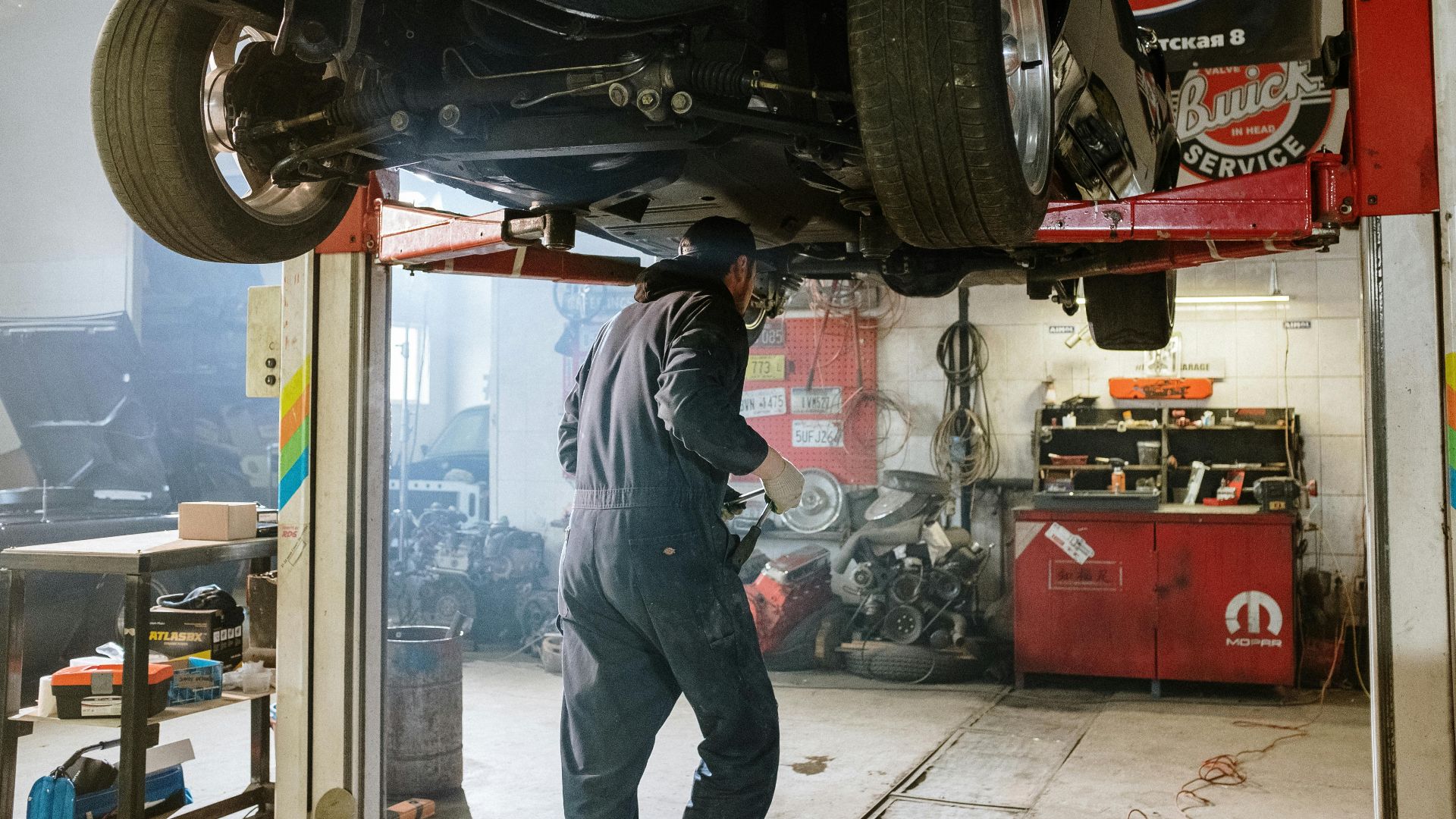 Mechanic repairing a vehicle in a busy workshop with various automotive tools.