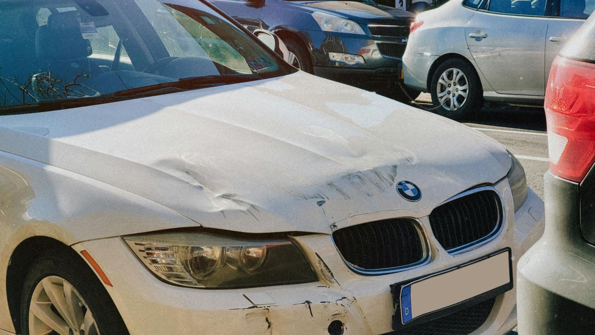 White BMW sedan with front-end damage parked on a busy city street.