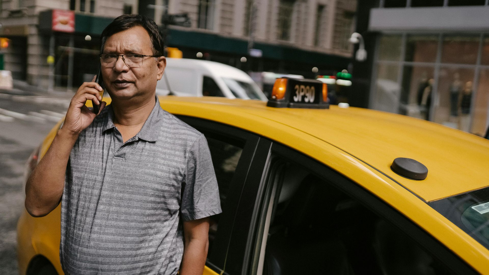 A confident taxi driver making a phone call in a bustling city street.
