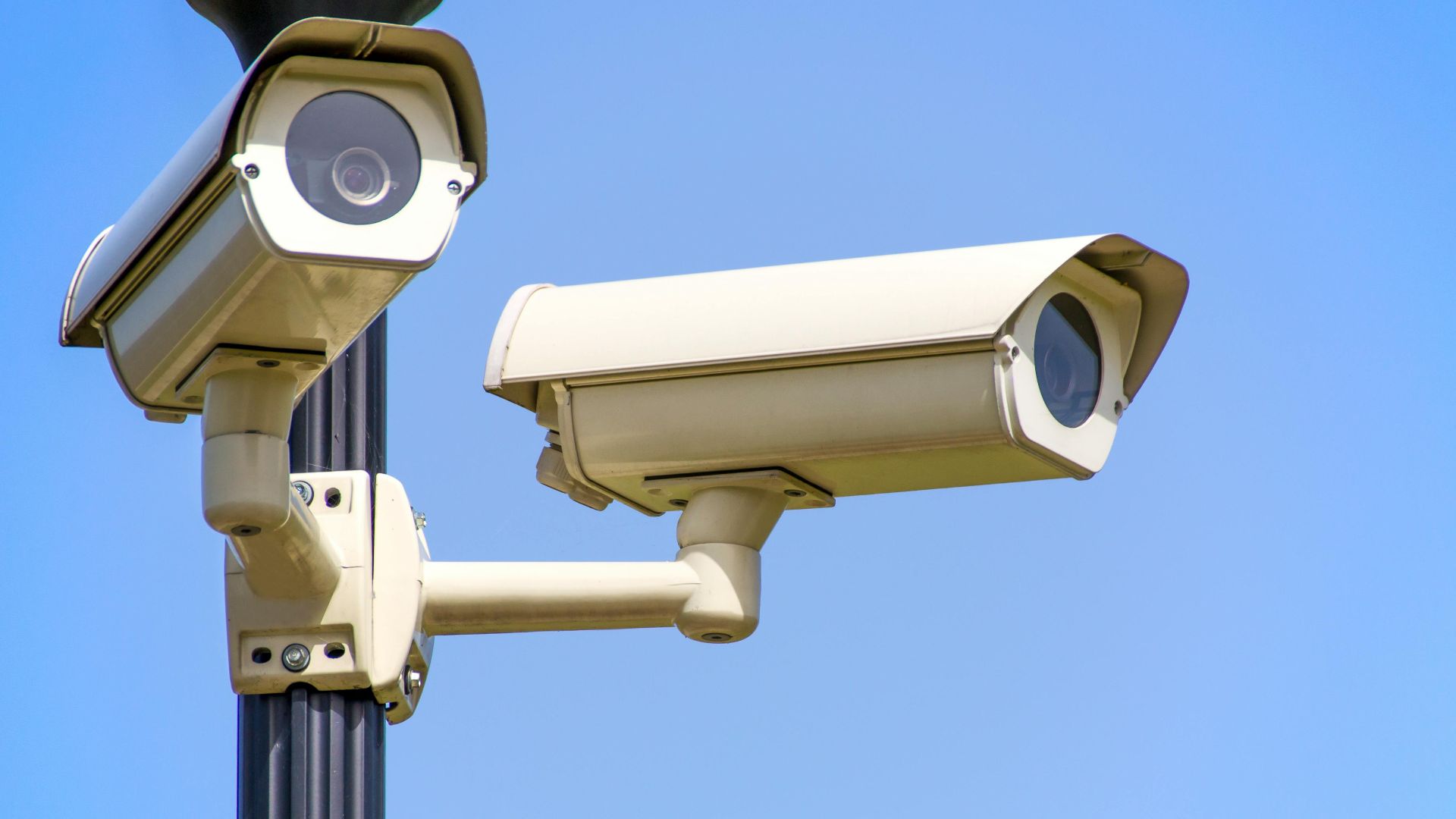 Outdoor security cameras mounted on a pole against a clear blue sky, ensuring vigilant surveillance.