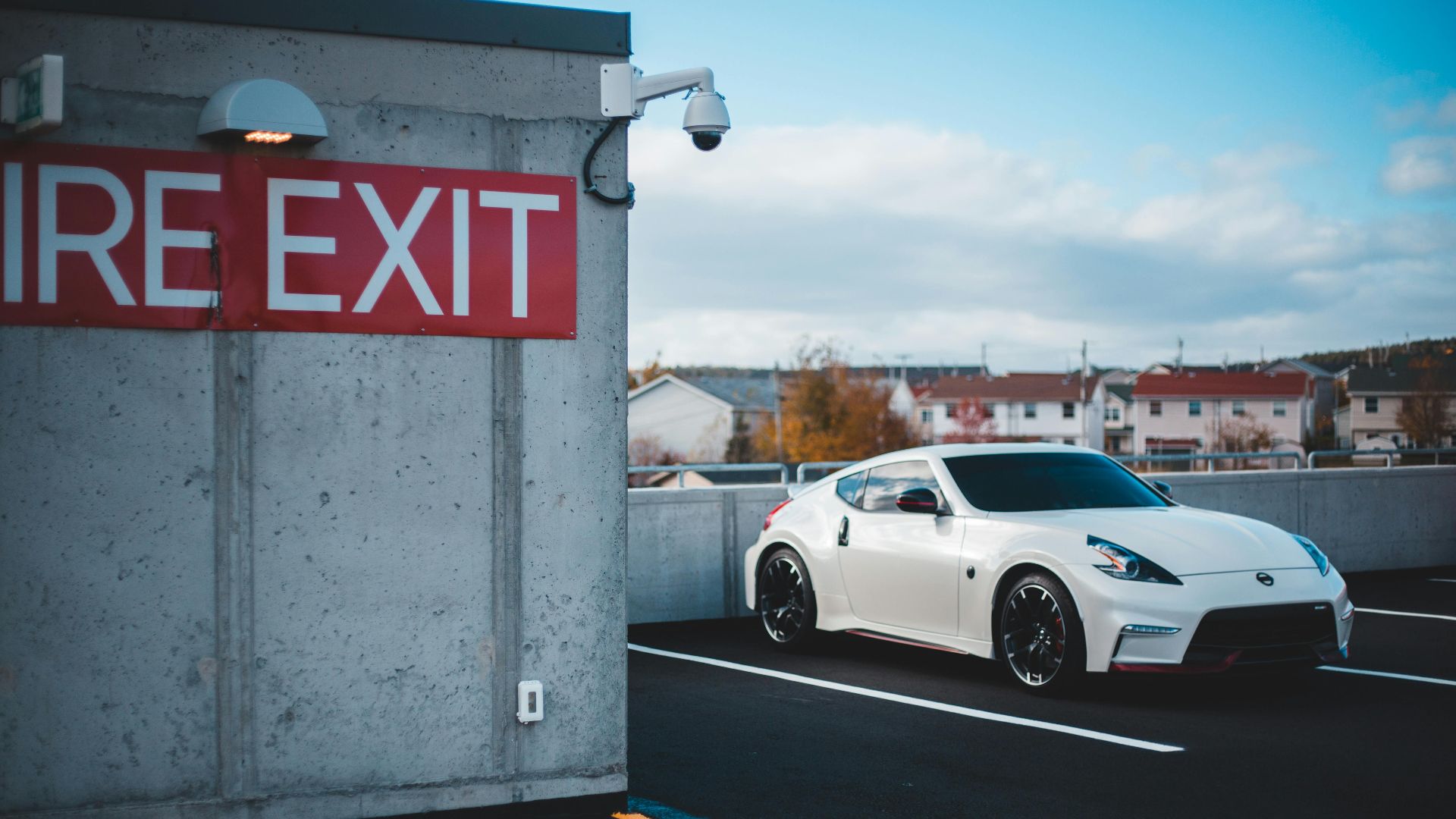 White sports car parked near a fire exit sign in a city parking lot.