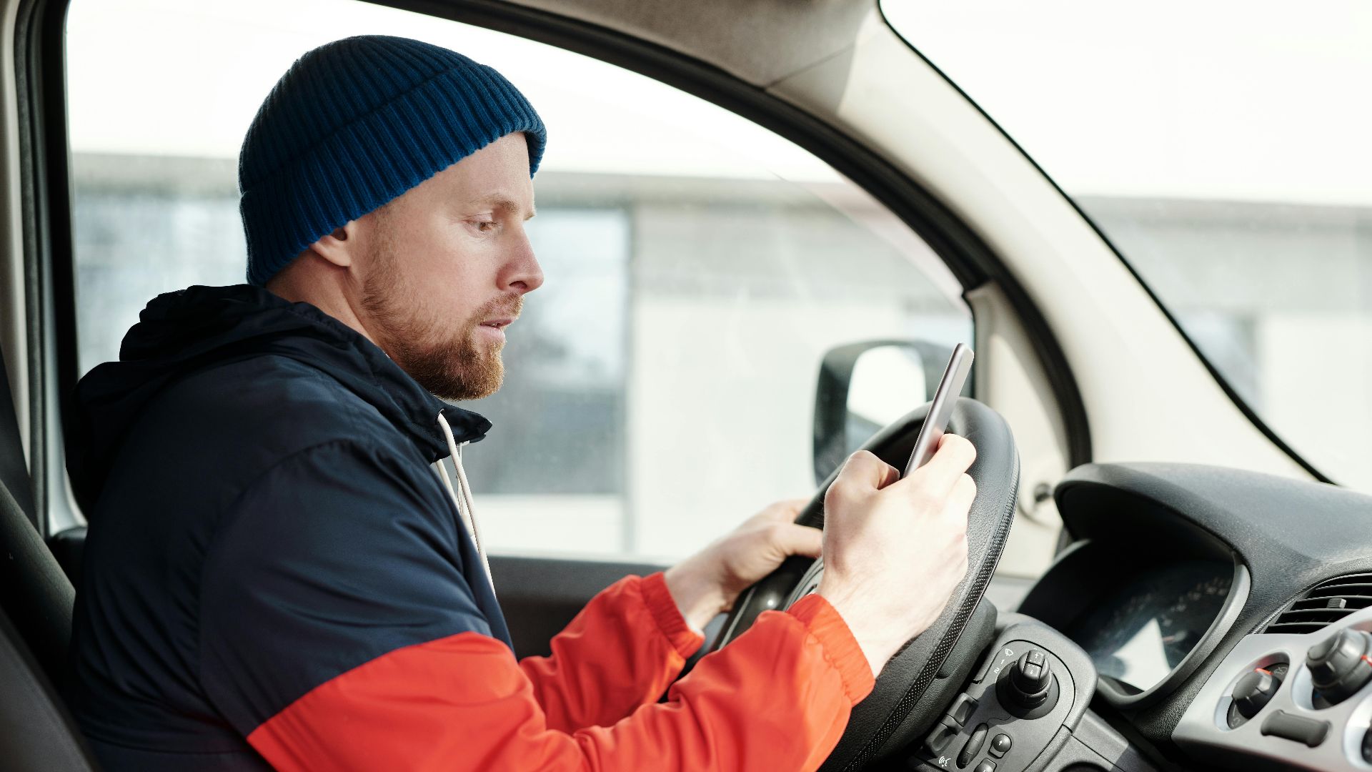 Distracted driver uses a smartphone in a car, highlighting road safety concerns.