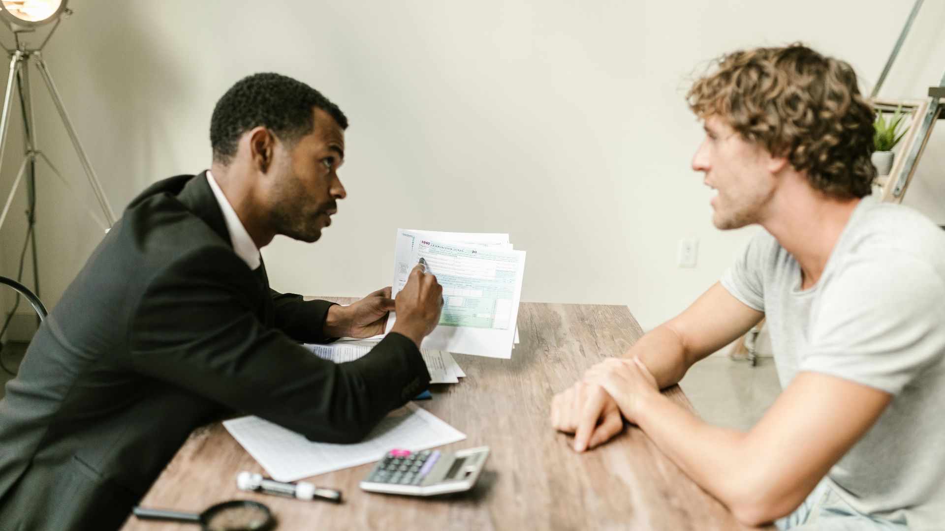 A financial advisor discusses paperwork with a client at a desk in a modern office.