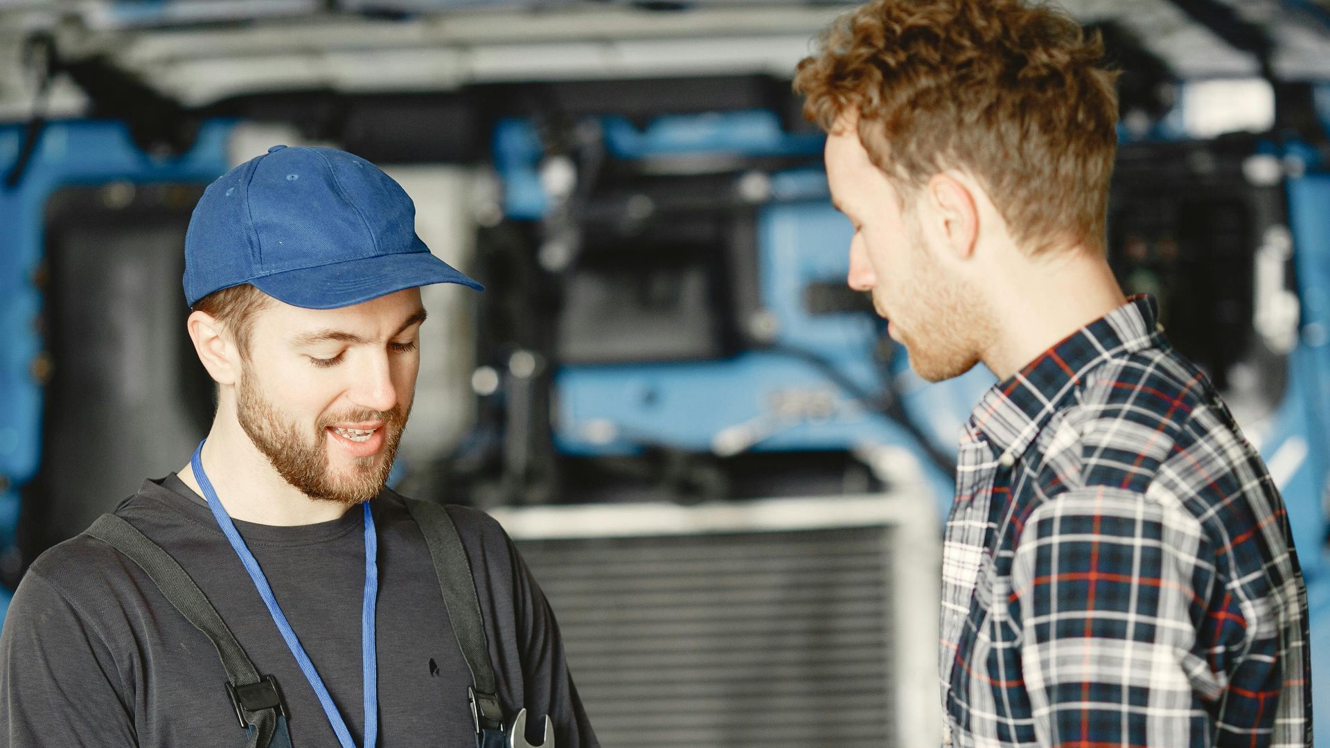 Auto mechanic in blue uniform receives payment from customer in a garage setting with a truck in the background.