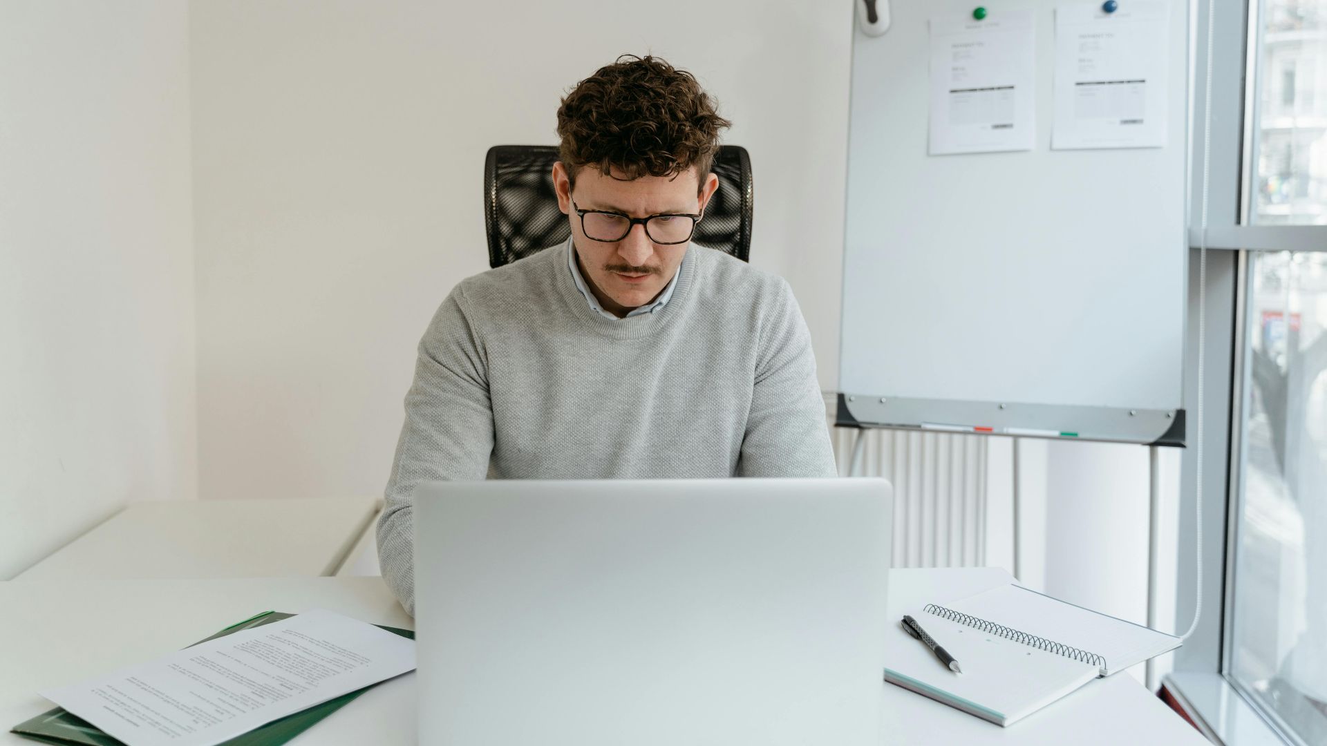 A serious businessman in a gray sweater focused on work at his modern office desk.