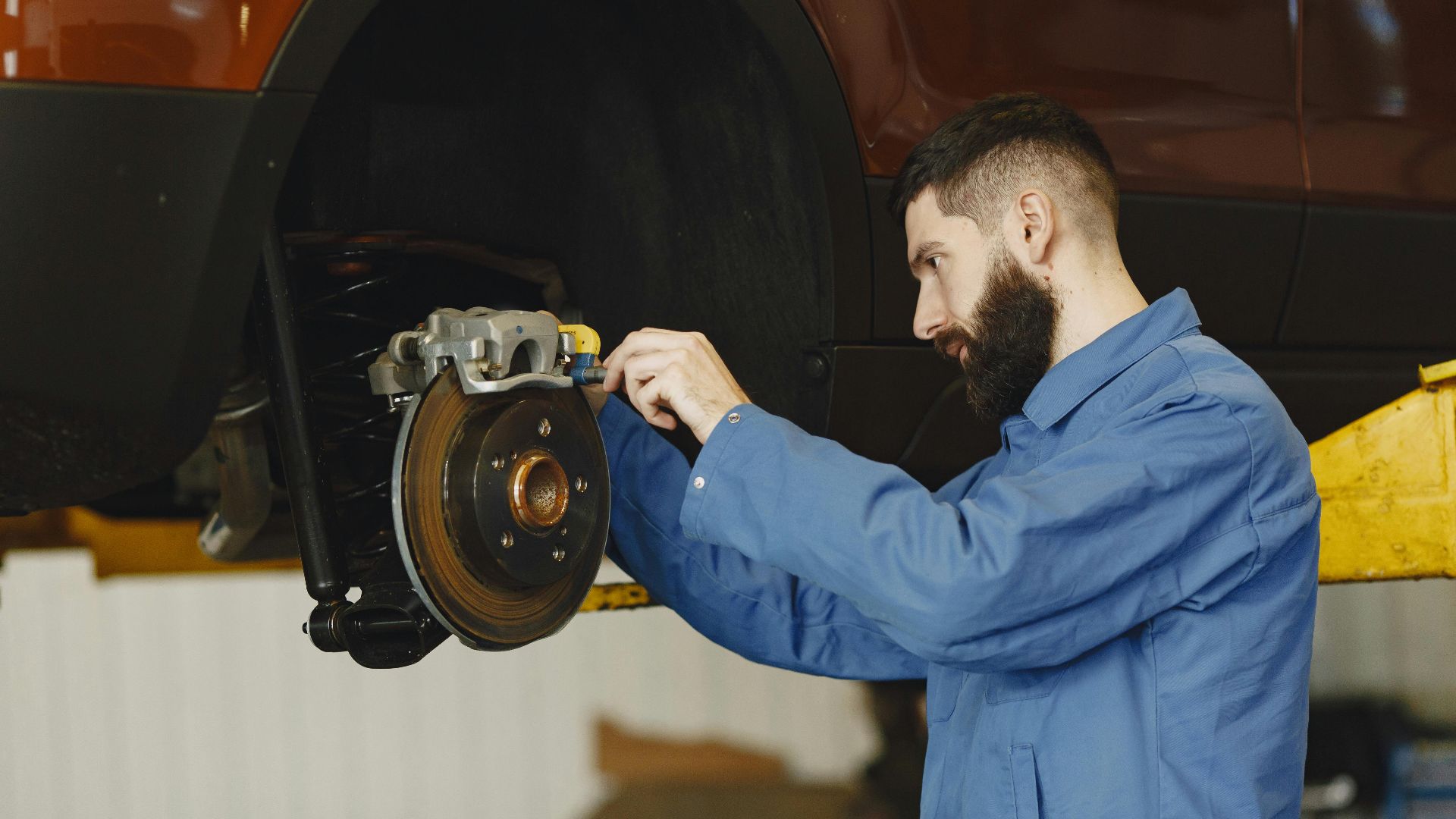 Mechanic in blue uniform performing brake repair on car in modern garage.