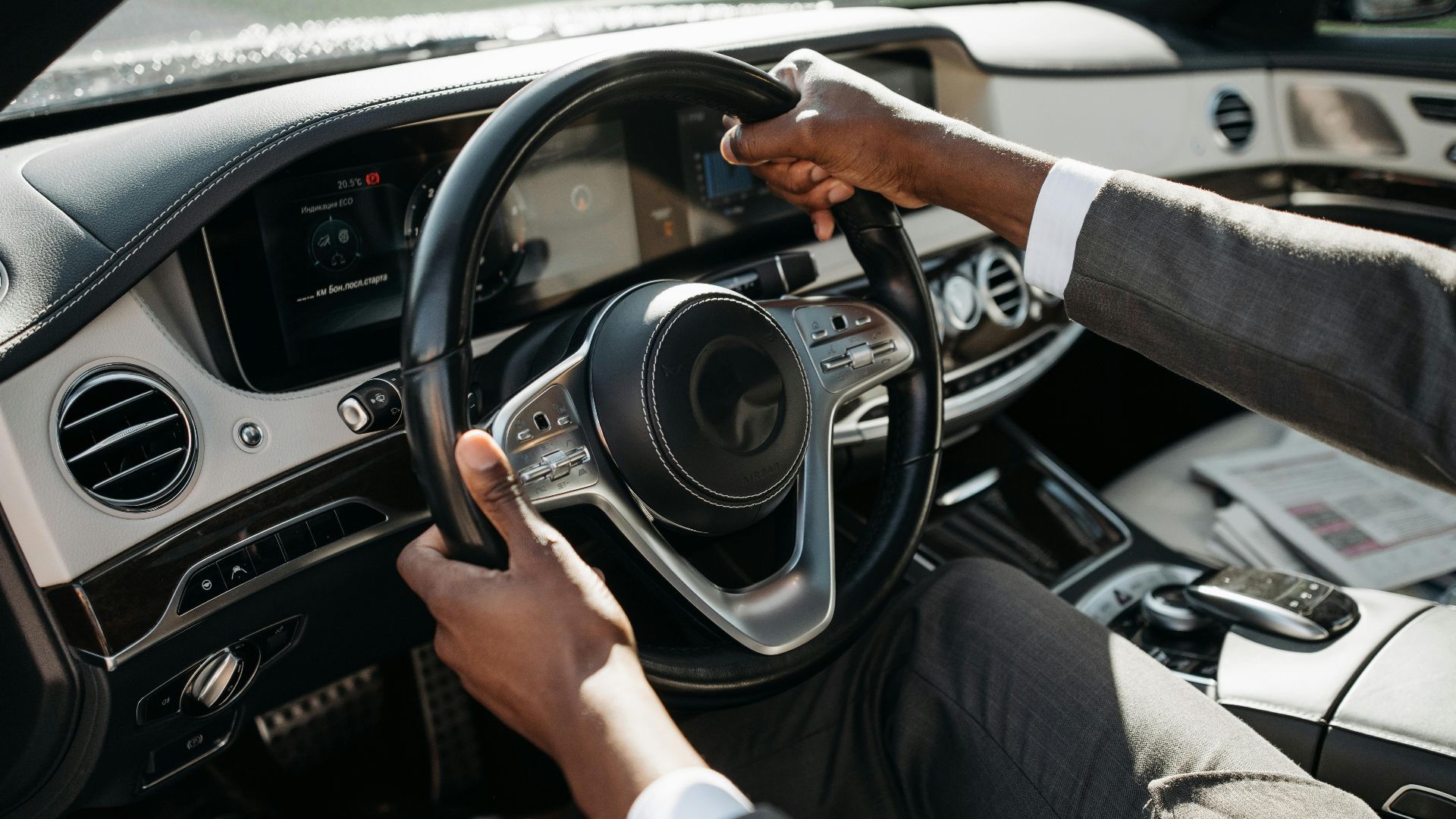 Close-up of hands on steering wheel in a luxury car with dashboard and controls.