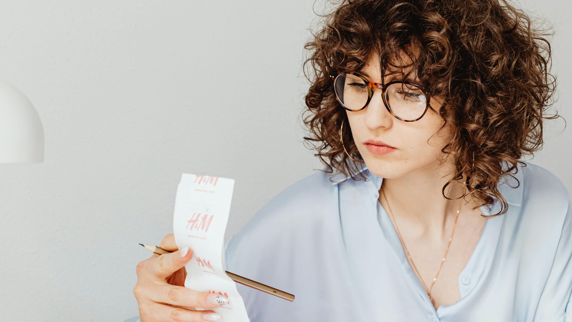 Curly-haired woman examining receipts with a calculator at her desk.