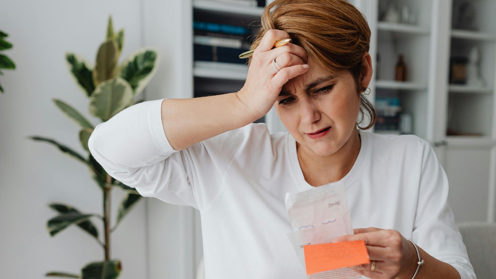 A businesswoman in an office looks frustrated while reviewing bills and finances with a laptop, displaying anxiety.