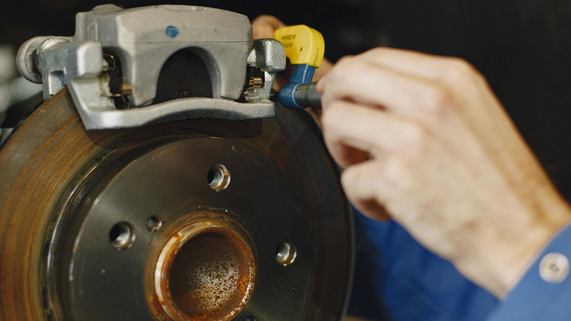 Mechanic working on car disc brake, inspecting for wear and maintenance.