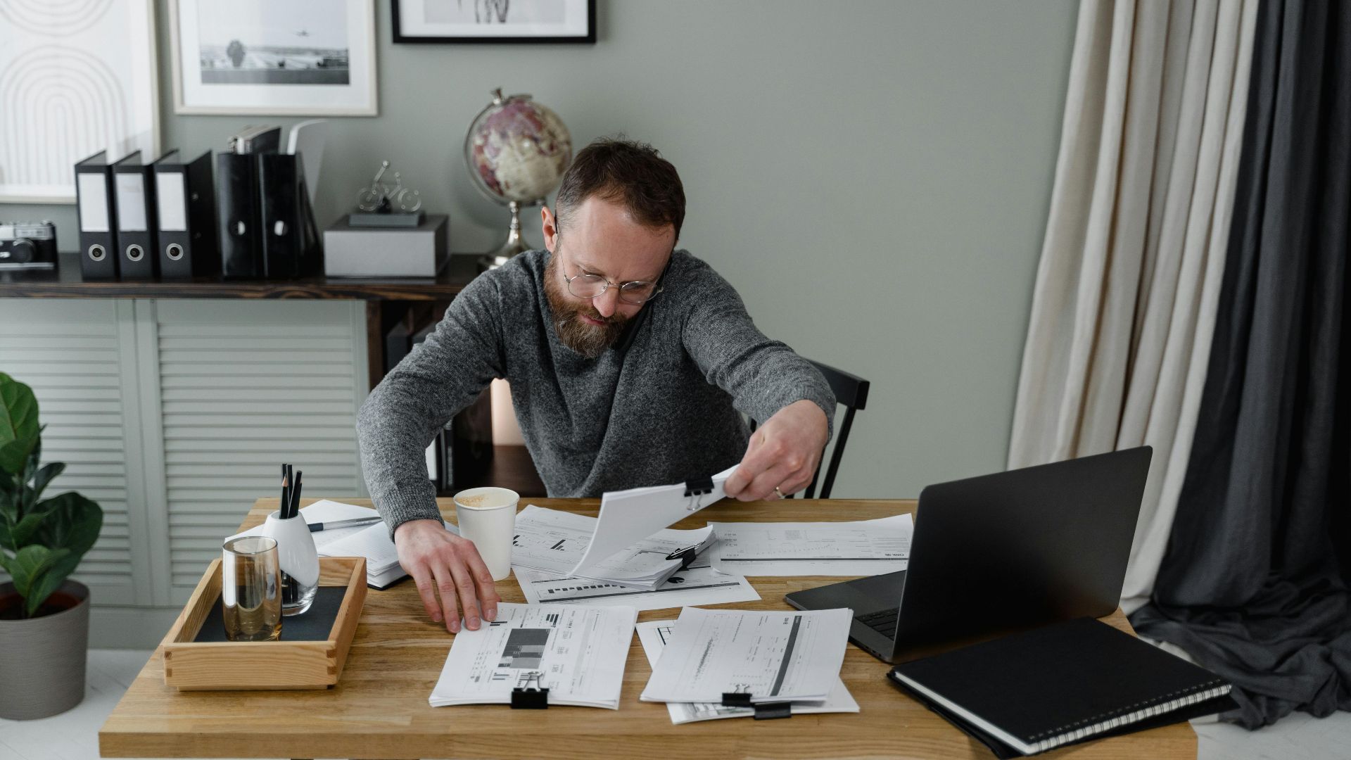 Professional reviewing documents at an office desk with a laptop and coffee.
