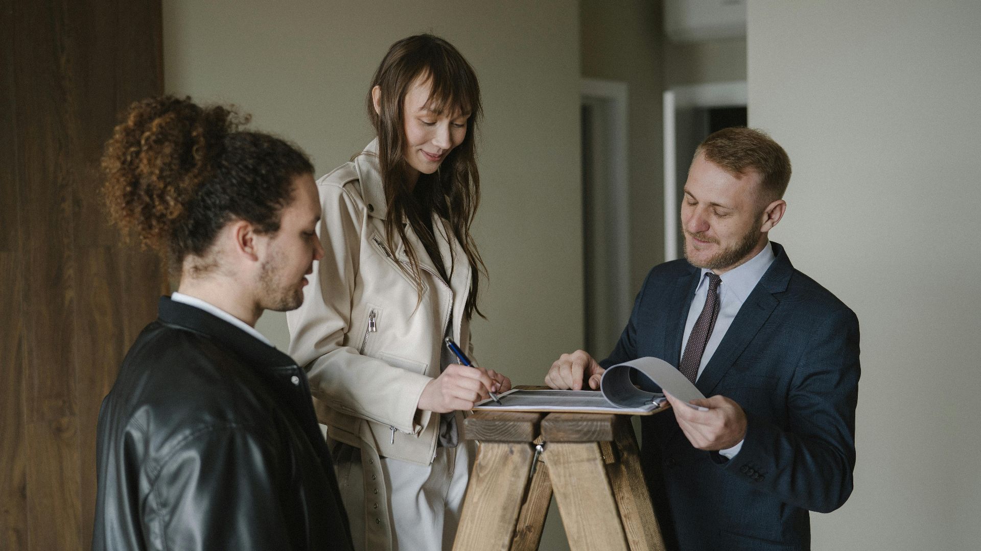 A couple signing real estate documents with a realtor inside a new apartment.