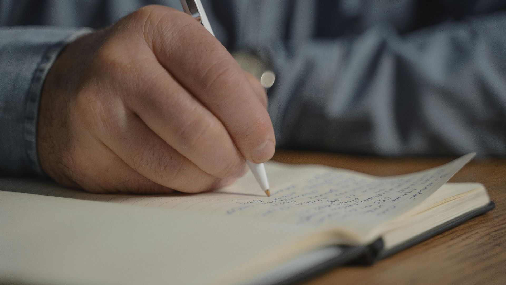 A close-up image of a hand writing with a pen in a notebook, creating a personal diary entry.