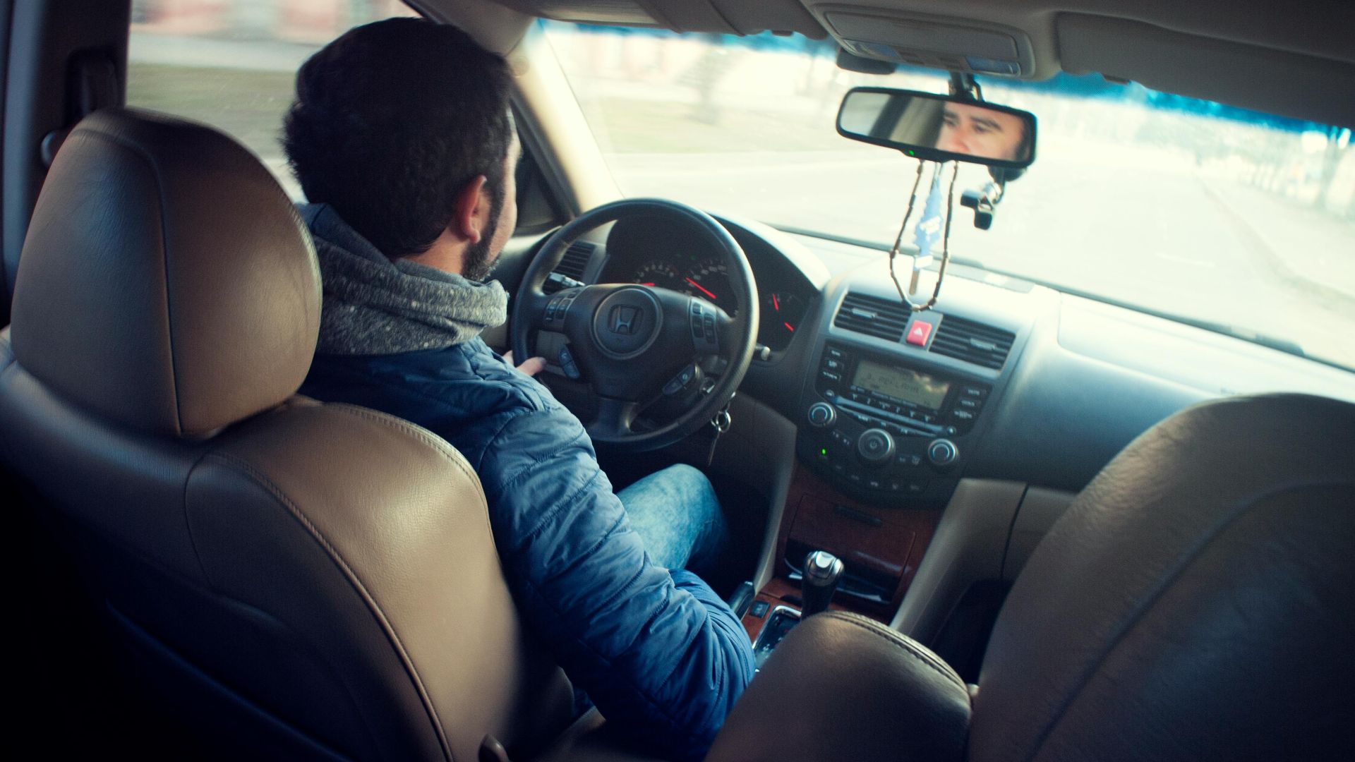 A man driving a car with focus on interior, dashboard, and steering wheel, captured from the backseat.