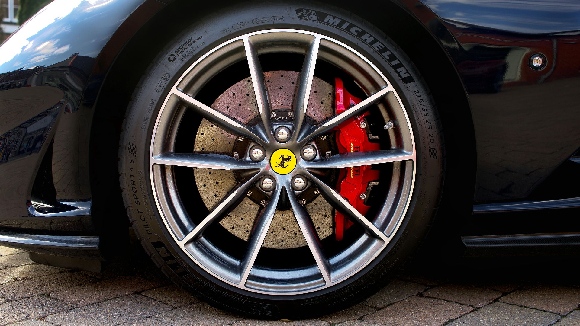 Detailed image of a Ferrari sports car wheel with red brake caliper, shot outdoors.