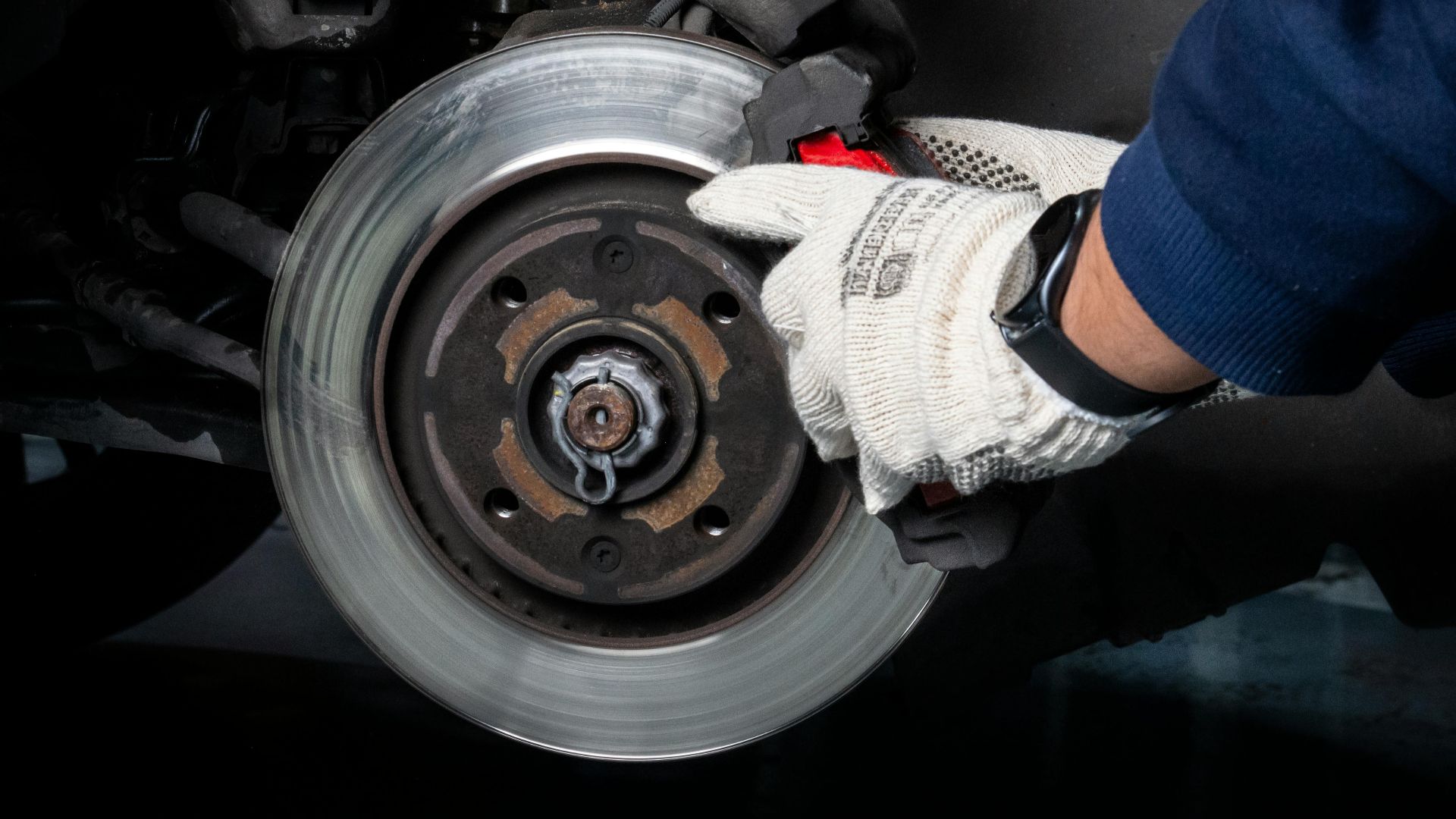 Mechanic working on car brake system in a workshop setting.