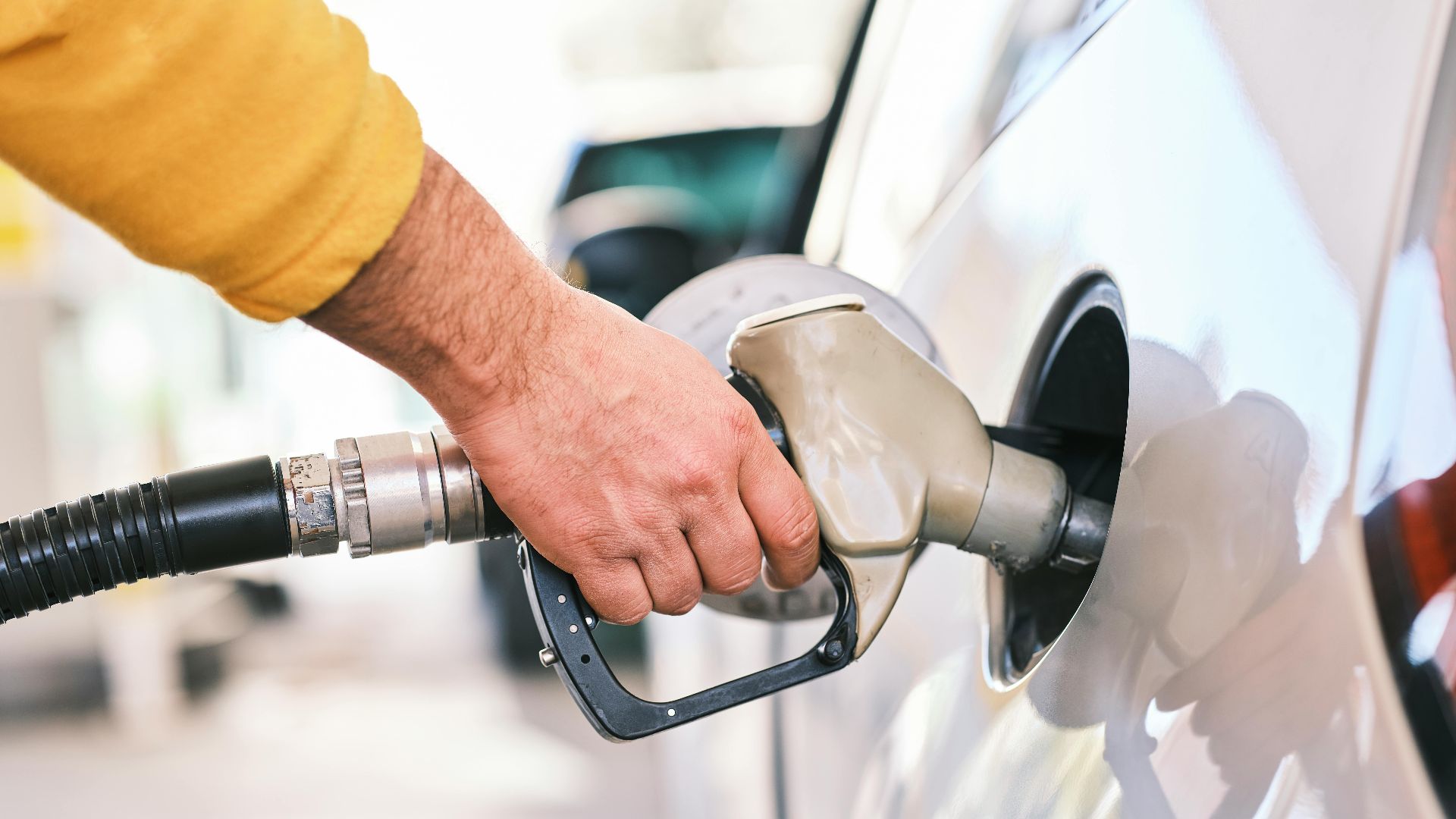 Close-up of a person refueling a car with a gas nozzle at a station.