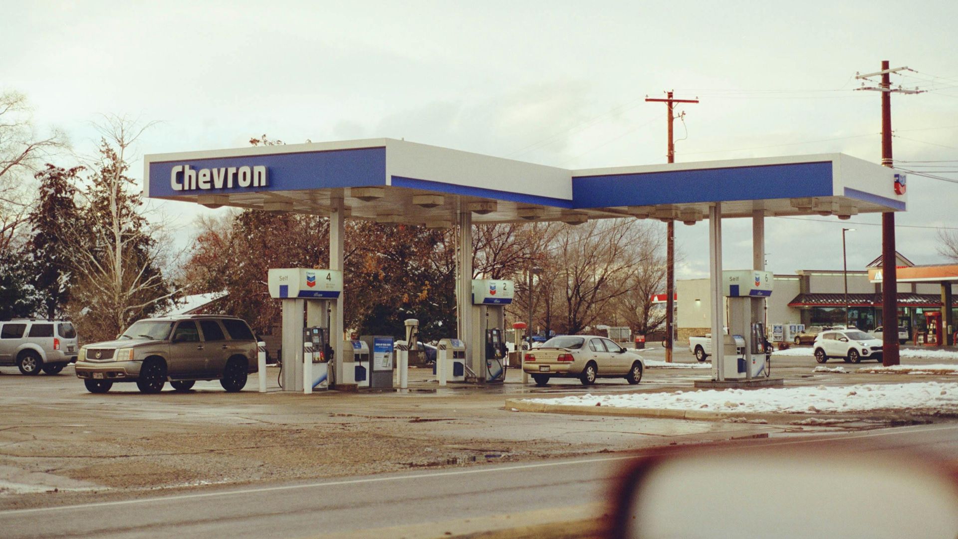 A Chevron gas station with several vehicles parked on a snowy day, emphasizing travel and fuel.