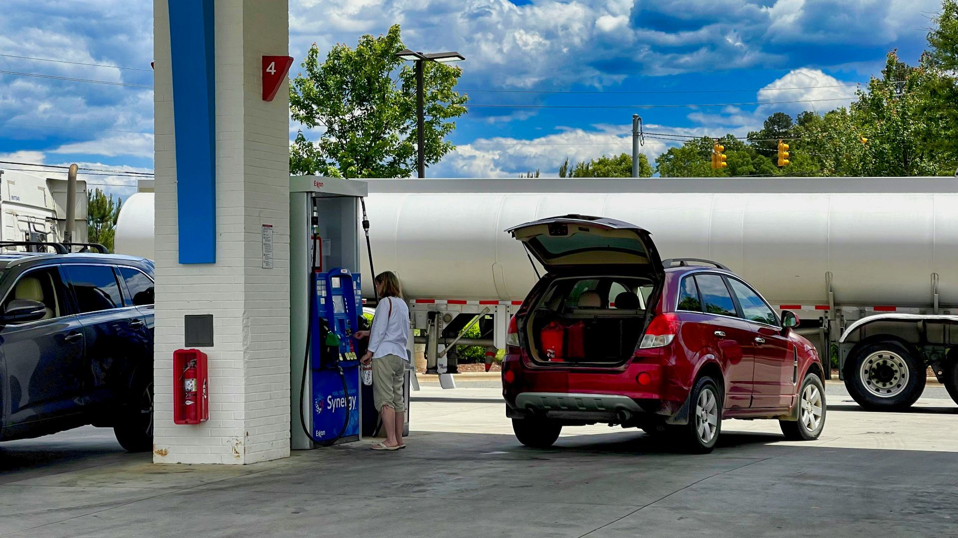man in white t-shirt standing beside red suv during daytime