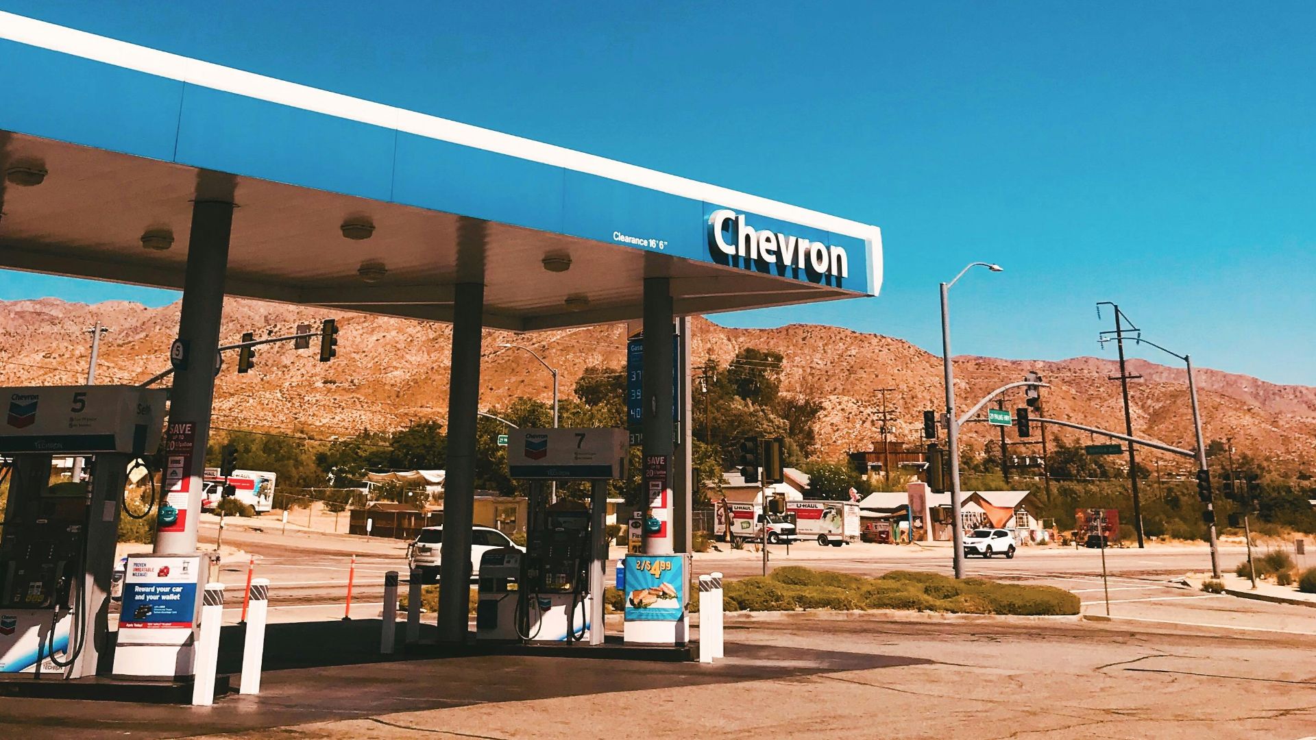 A Chevron gas station with mountains in the background under a clear blue sky in California, USA.
