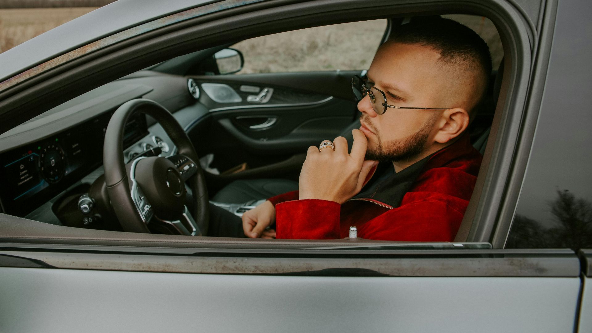 Side view of thoughtful young bearded male in eyeglasses sitting in driver seat of car