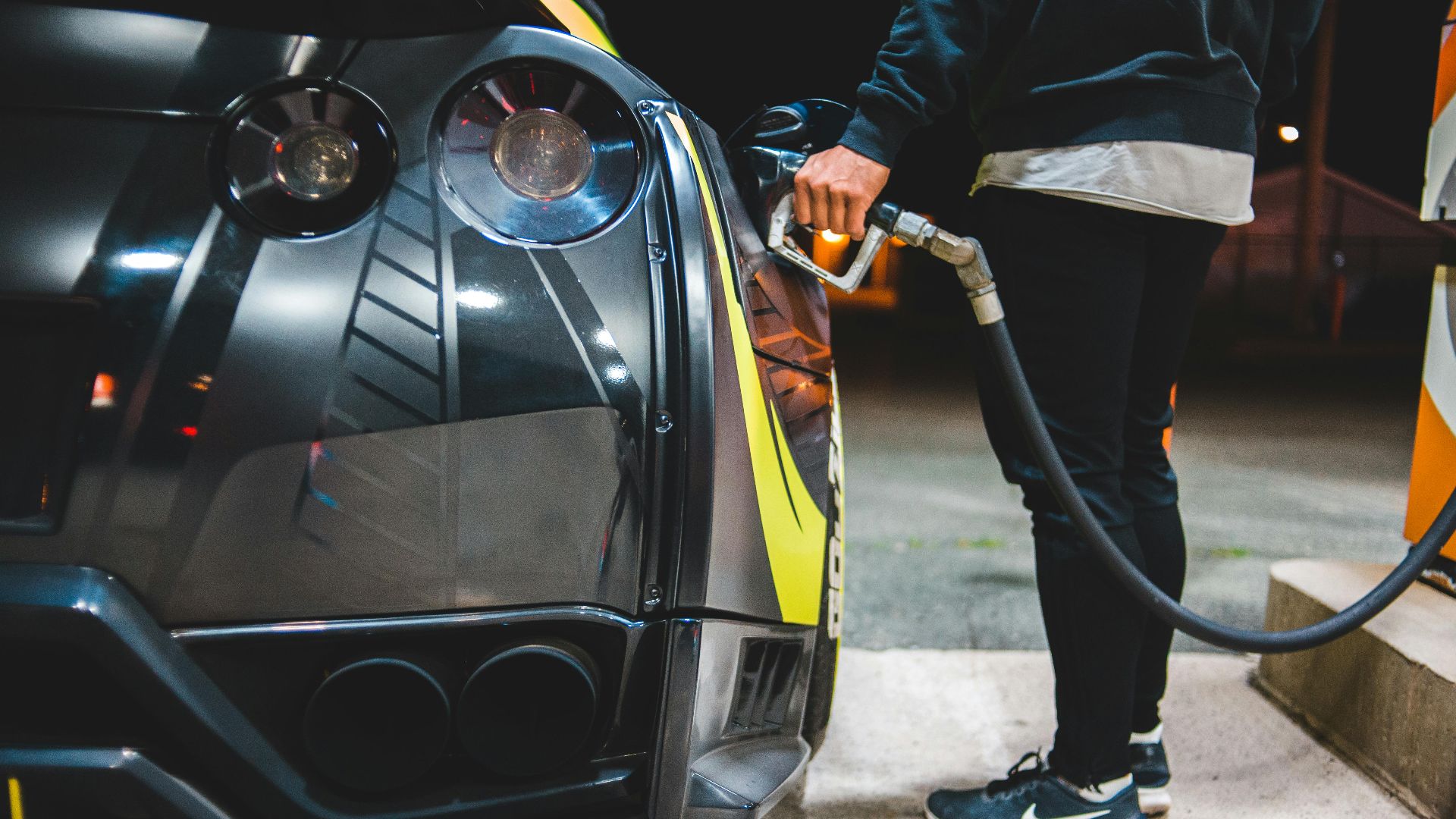 Side view of crop unrecognizable male refueling modern racing automobile in petrol station in evening