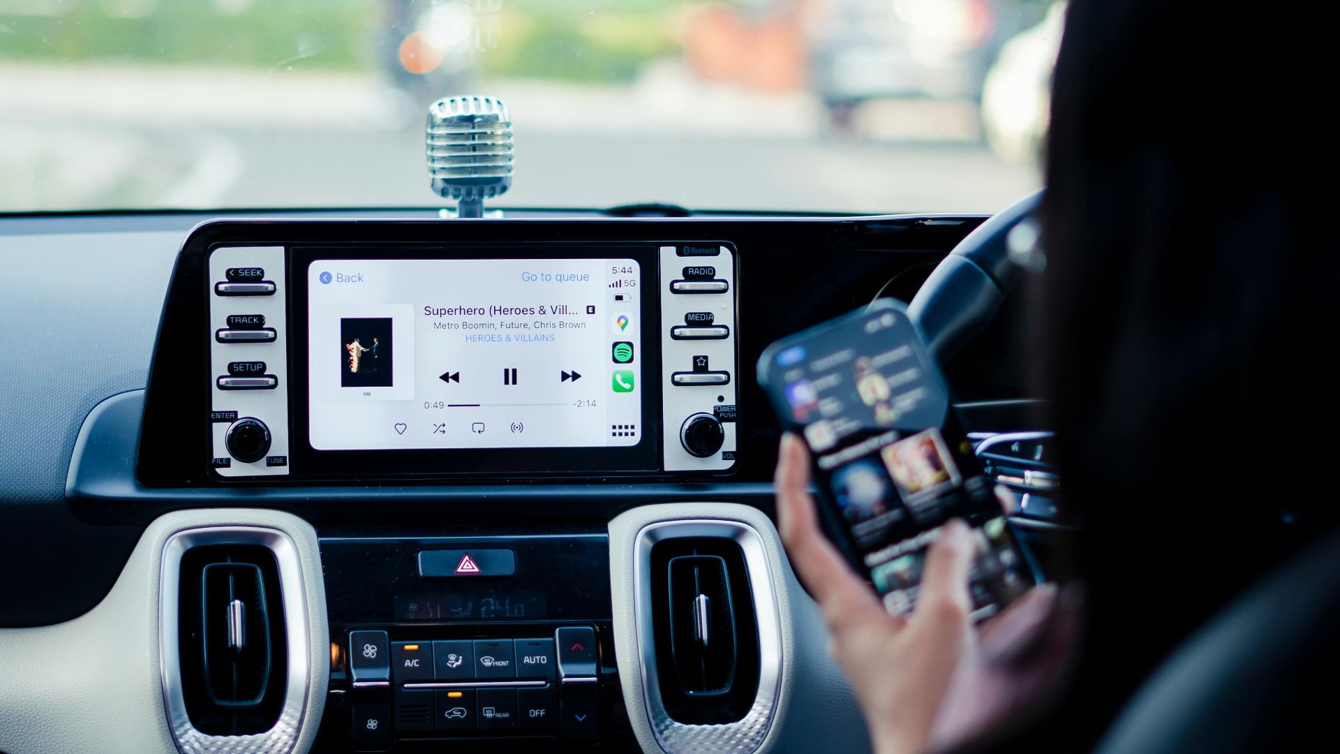 Car dashboard with a touchscreen display and person using a smartphone inside a vehicle.