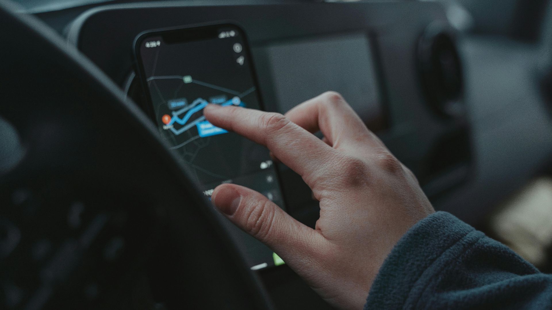 Hand interacting with GPS navigation on a smartphone mounted in a car interior.