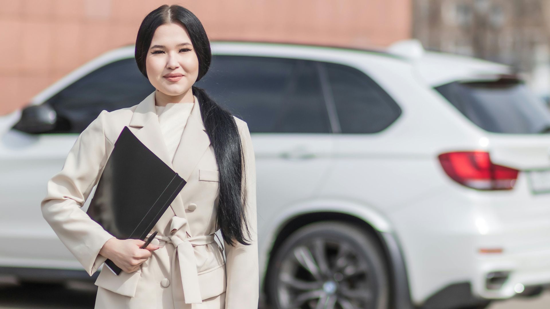 Smiling professional woman standing confidently by a luxury car, embodying success.