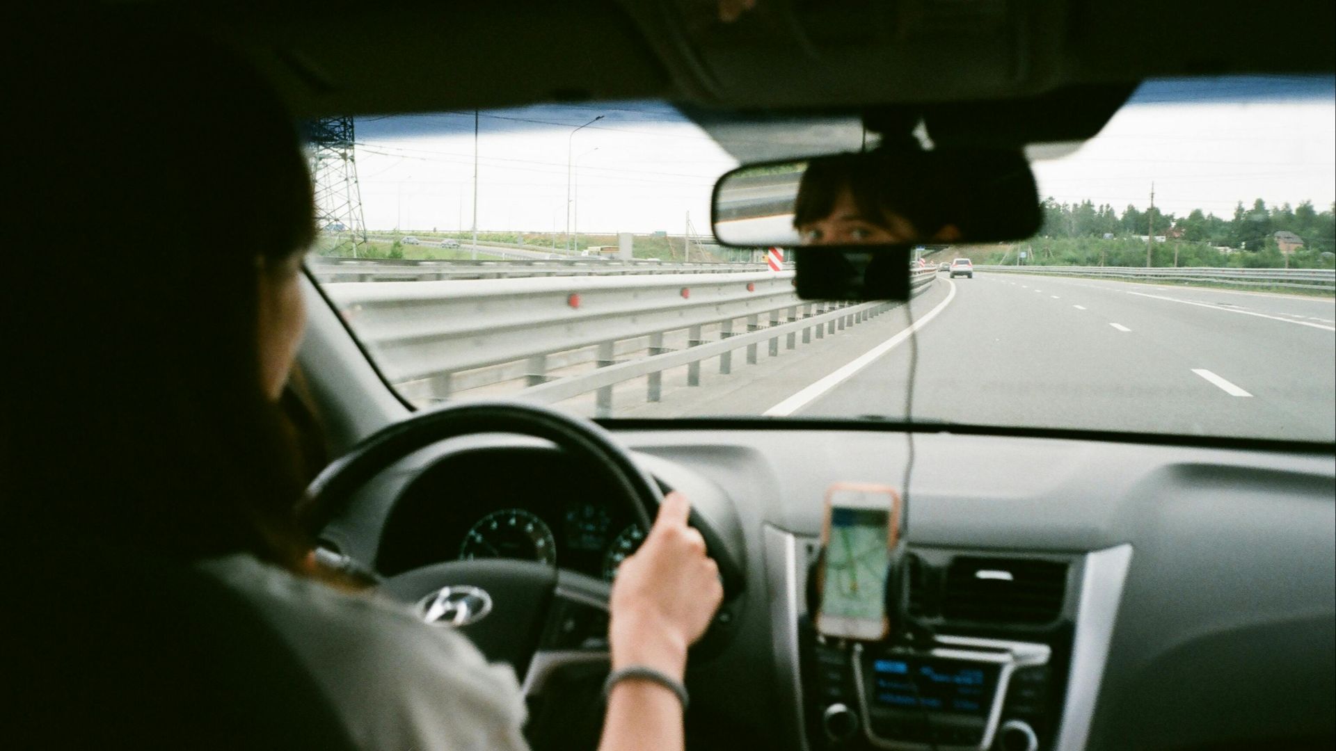 A woman driving a car on the highway, using GPS navigation on her smartphone.