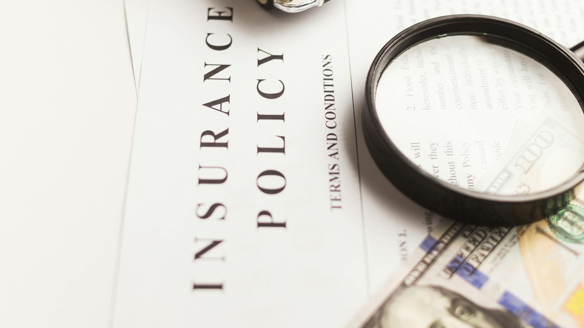 Close-up image of an insurance policy with a magnifying glass, money, and toy car.