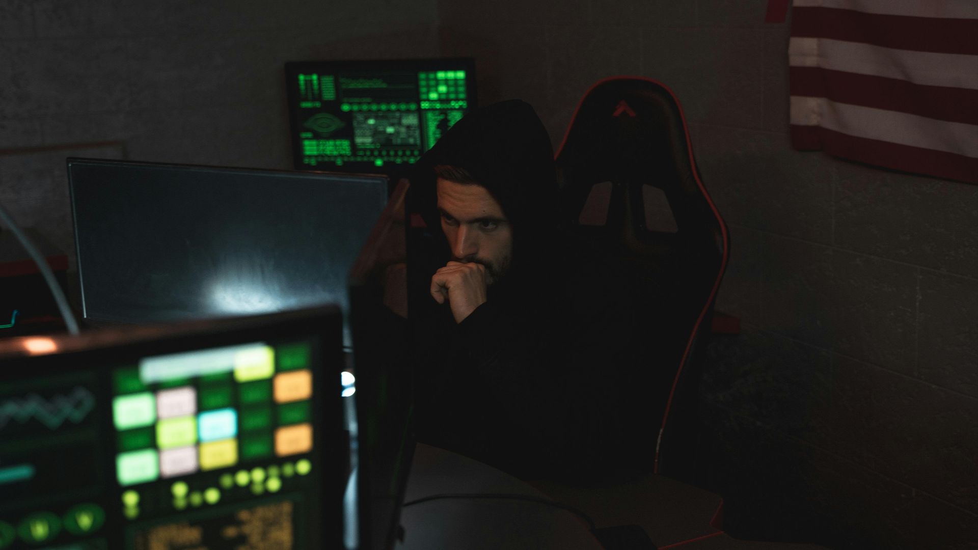 A cybersecurity expert monitors multiple screens, focused on data protection in a dark room.