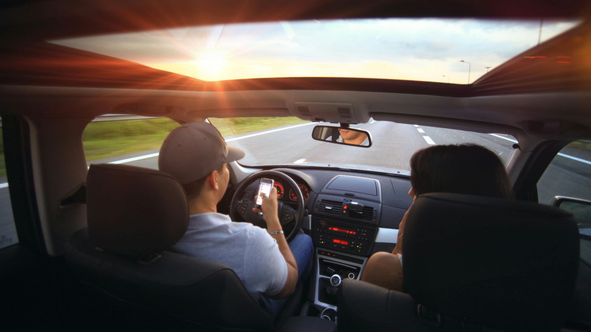Driver using phone while driving at sunset with passenger in vehicle.