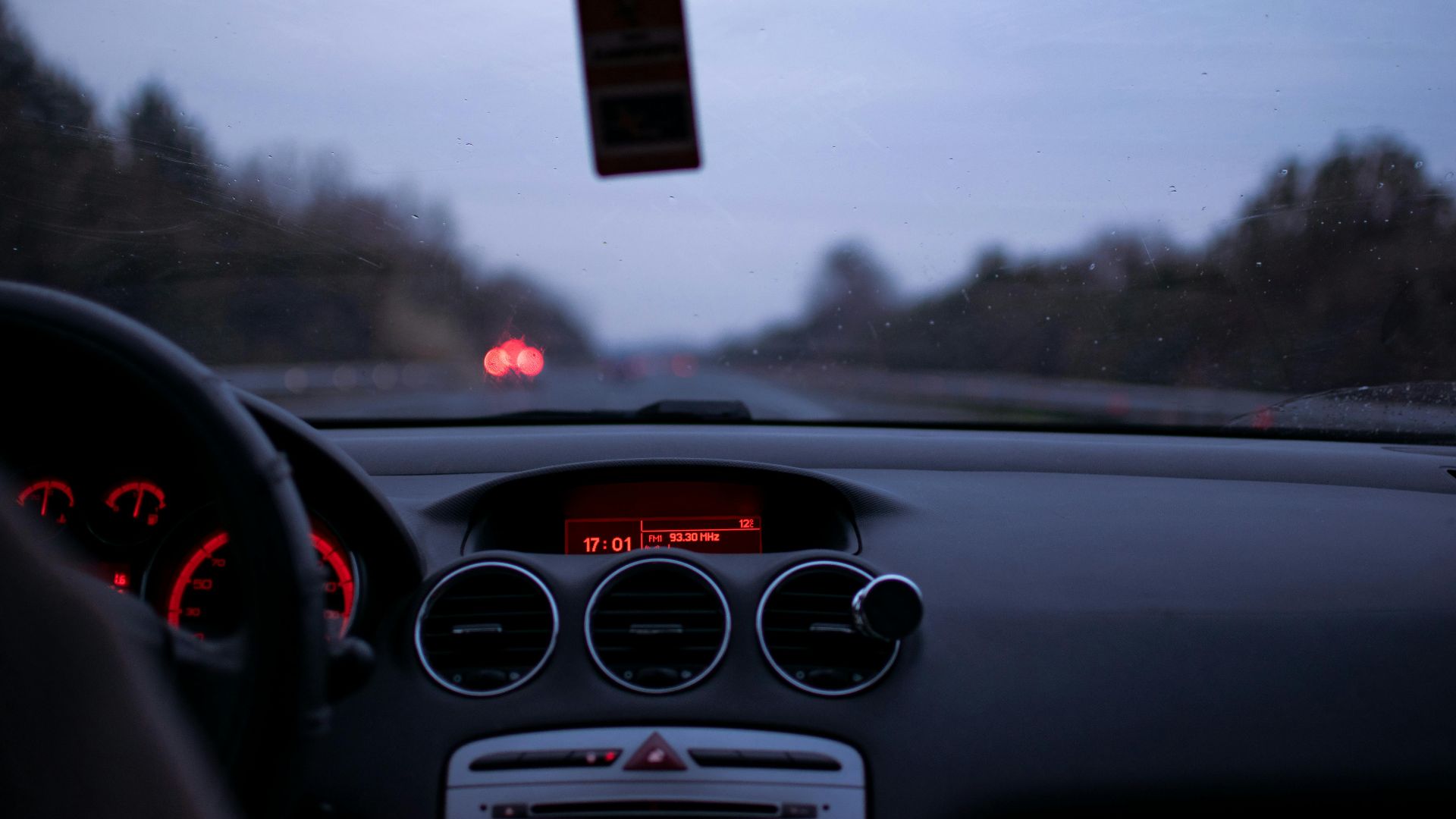 Car dashboard and windshield view on a highway at twilight with illuminated dials and road ahead.