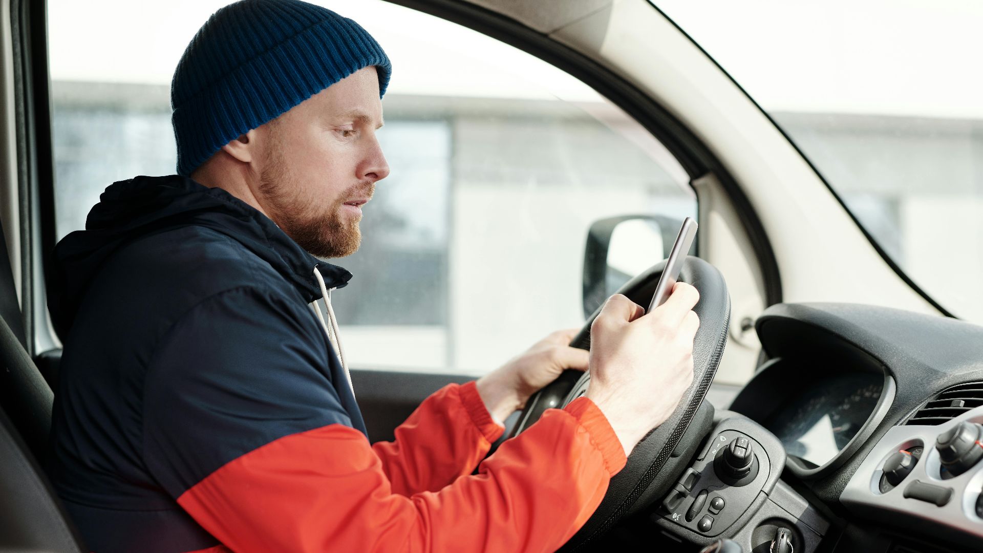 Distracted driver uses a smartphone in a car, highlighting road safety concerns.