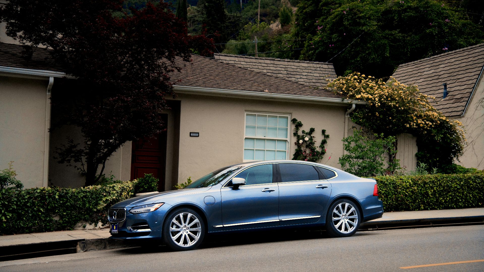 A sleek blue luxury car parked in front of a suburban house with greenery.