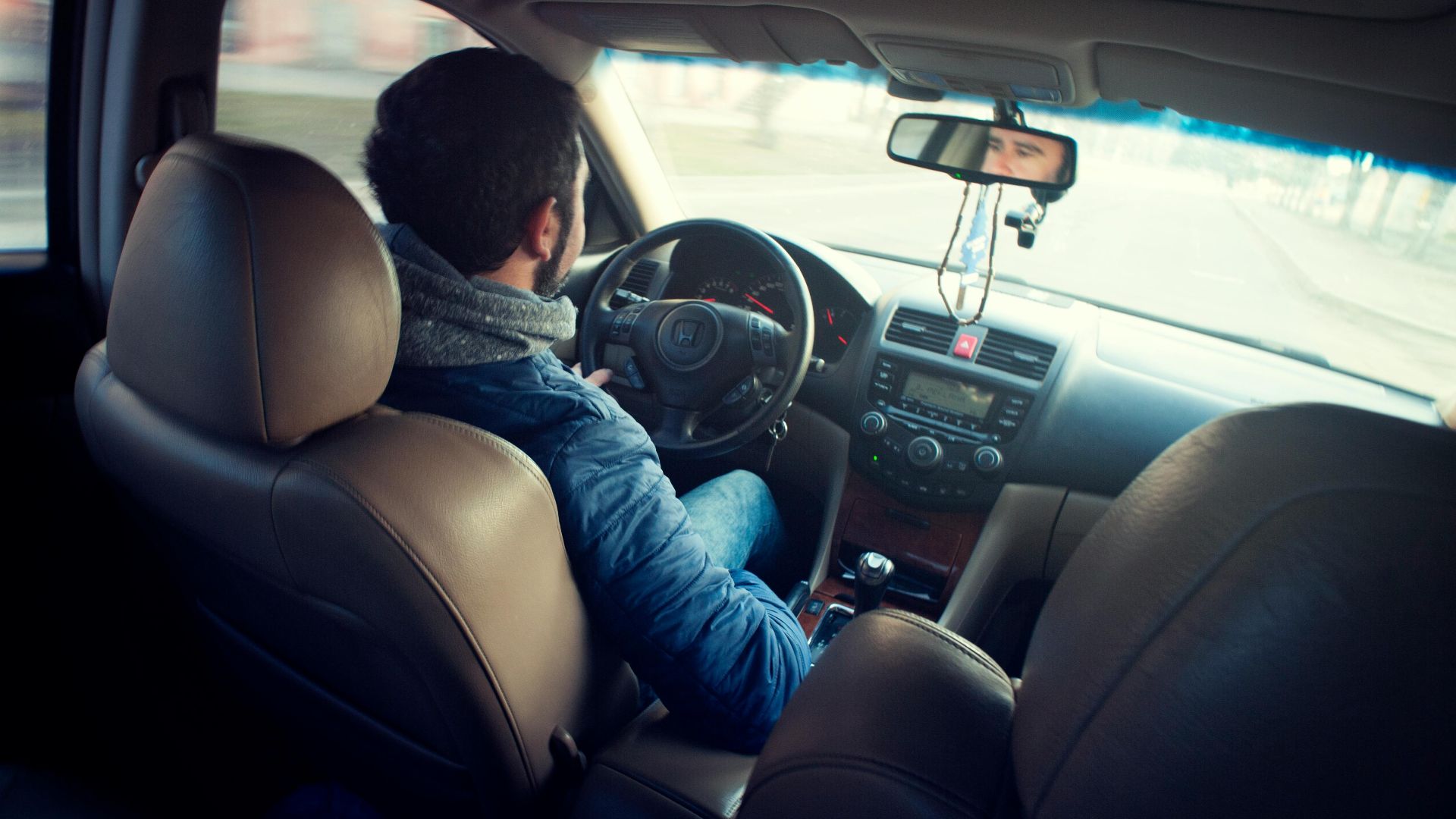 A man driving a car with focus on interior, dashboard, and steering wheel, captured from the backseat.