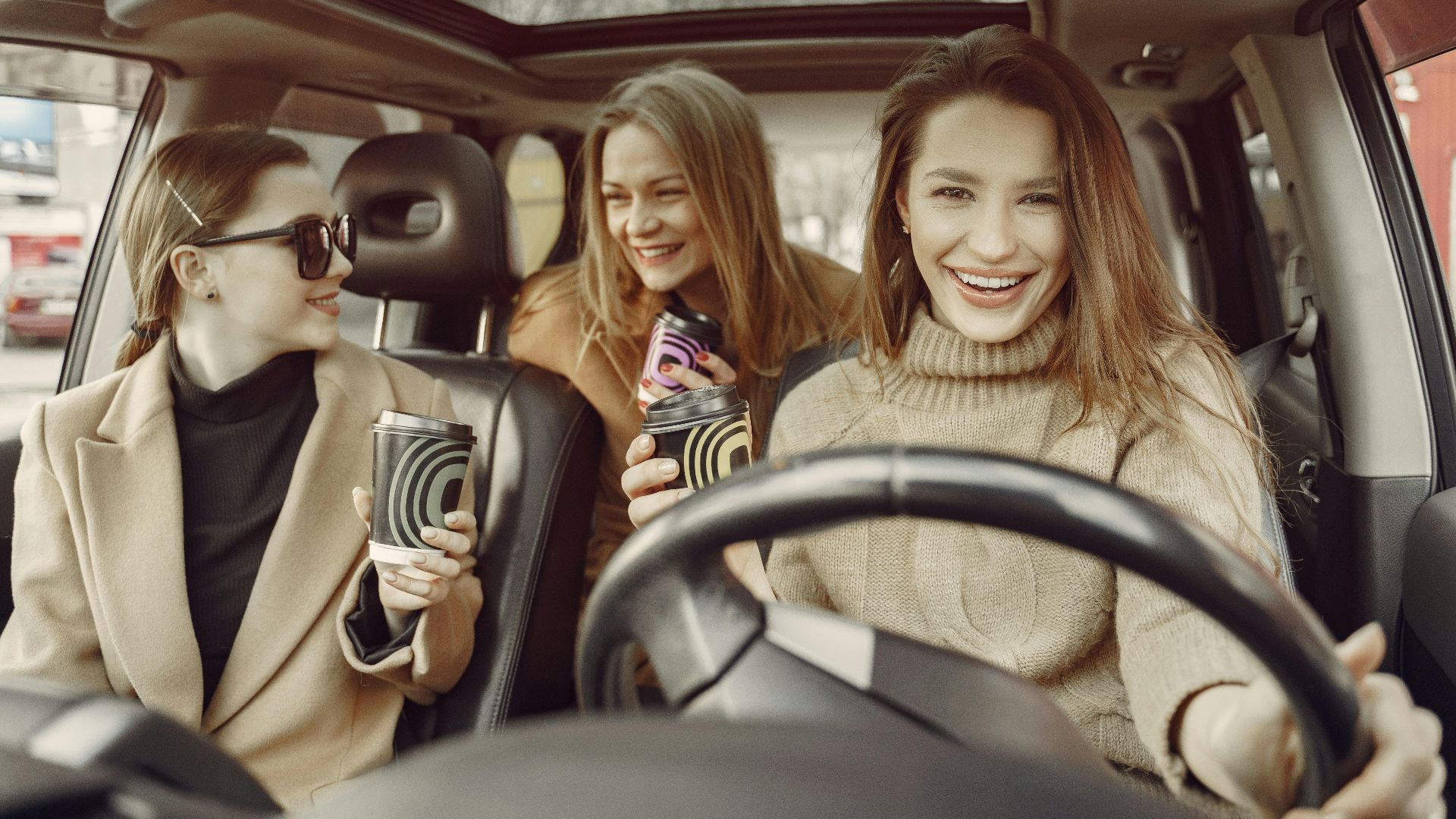 Happy friends relaxing with takeaway coffee in a car, sharing laughter and enjoyment on a casual day out.