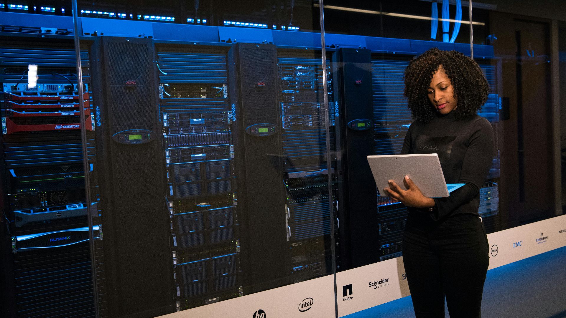 A female engineer using a laptop while monitoring data servers in a modern server room.