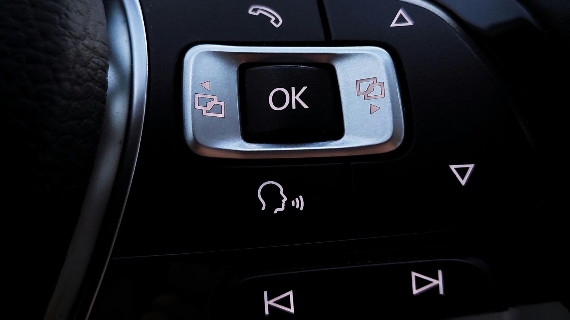 Detailed view of modern car steering wheel buttons with voice command icons and navigation arrows.