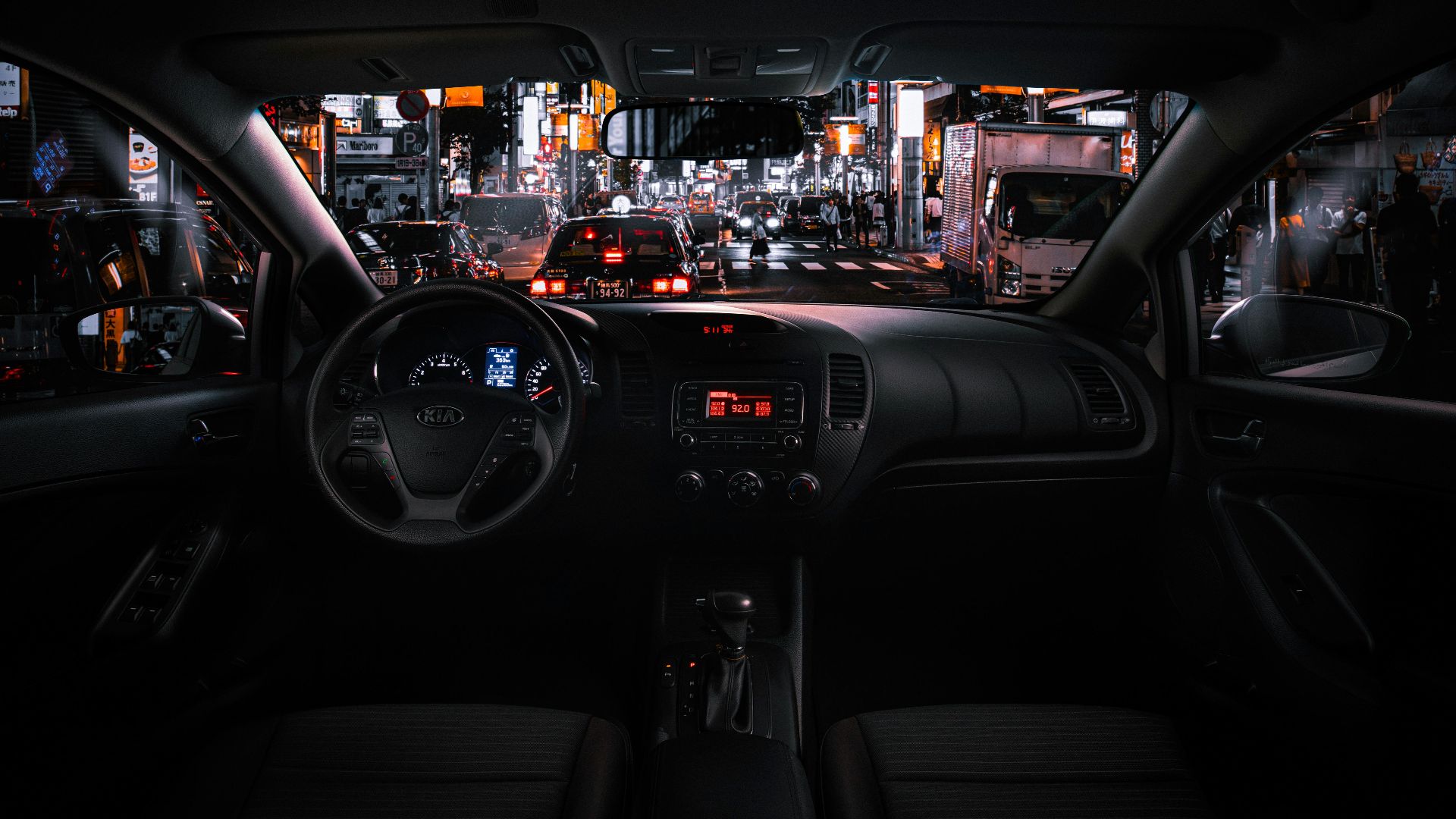 View from car interior at night in Tokyo, featuring bustling street traffic and illuminated cityscape.
