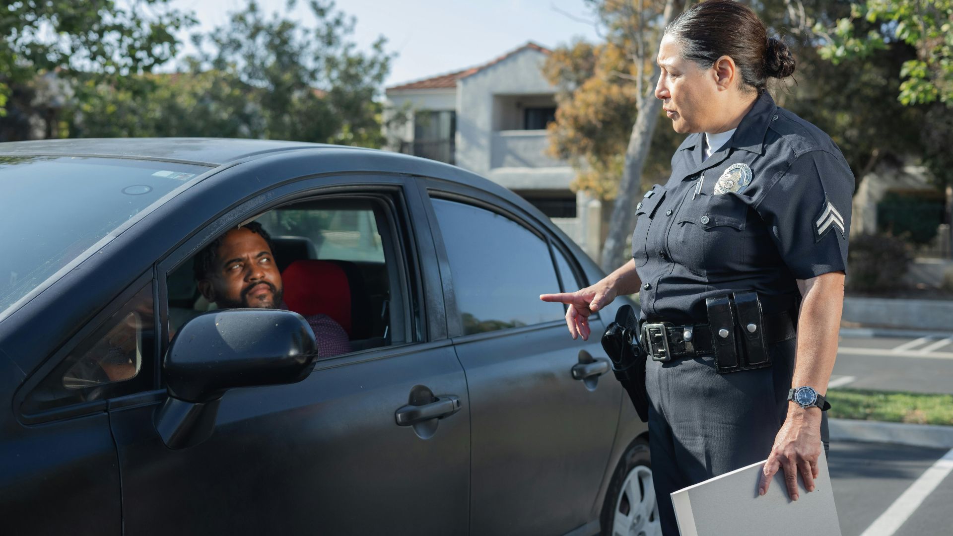 A police officer interacts with a driver during a daytime traffic stop on a residential street.