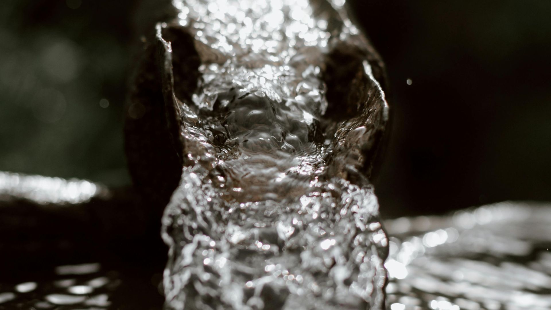 Close-up of water flowing through metal pipe outdoors, showcasing motion and texture.