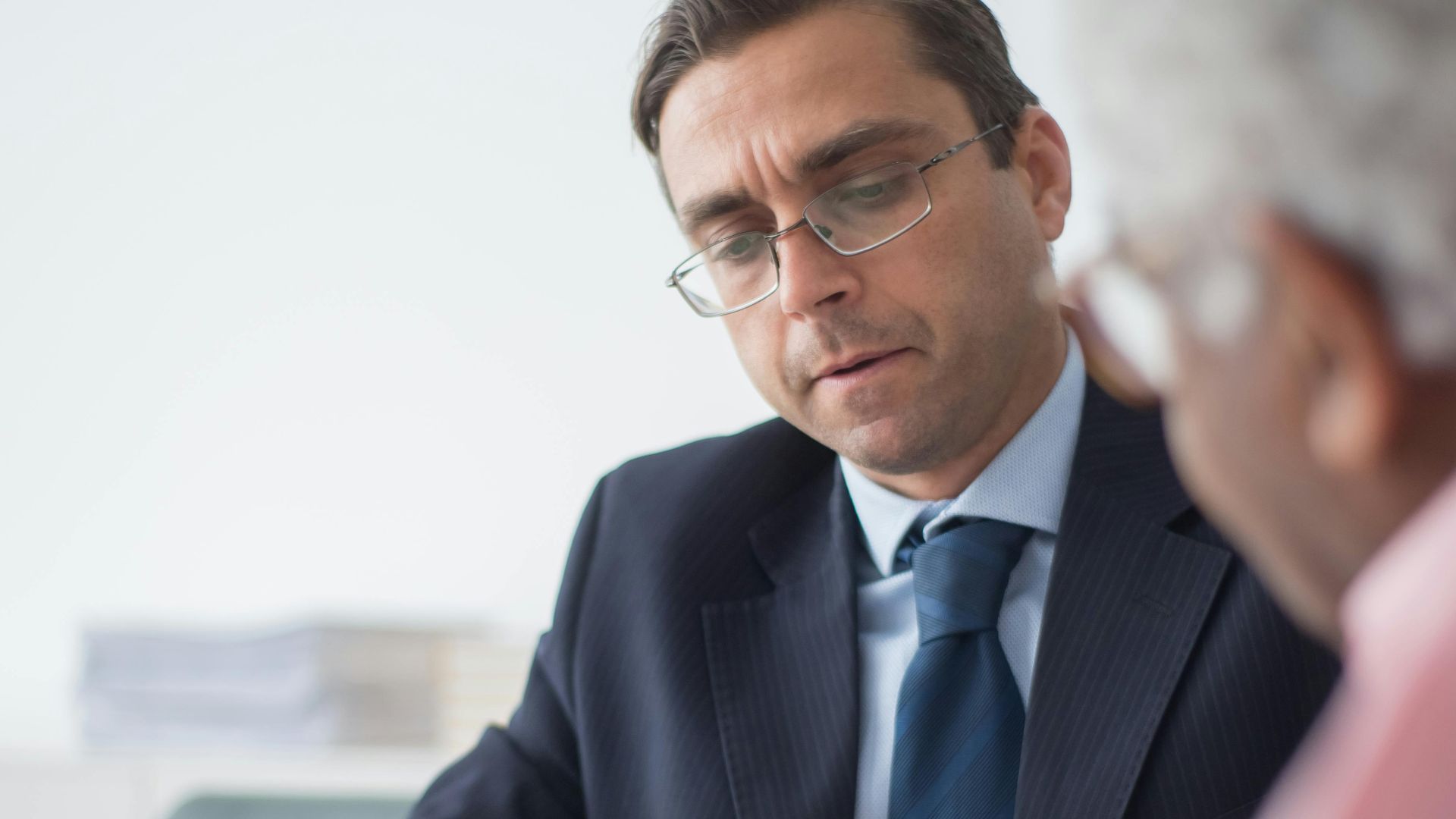 Senior man in discussion with consultant in office setting, reviewing documents.