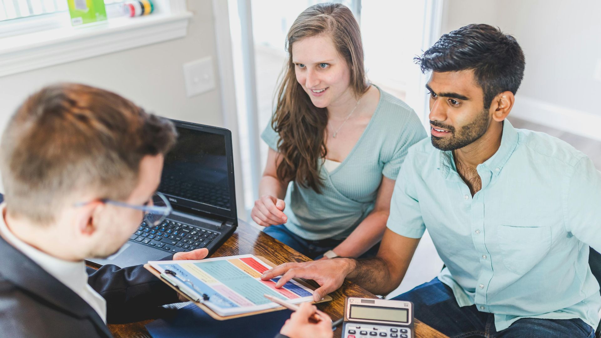 A couple consults with a real estate agent about buying a new home, papers and calculator on the table.