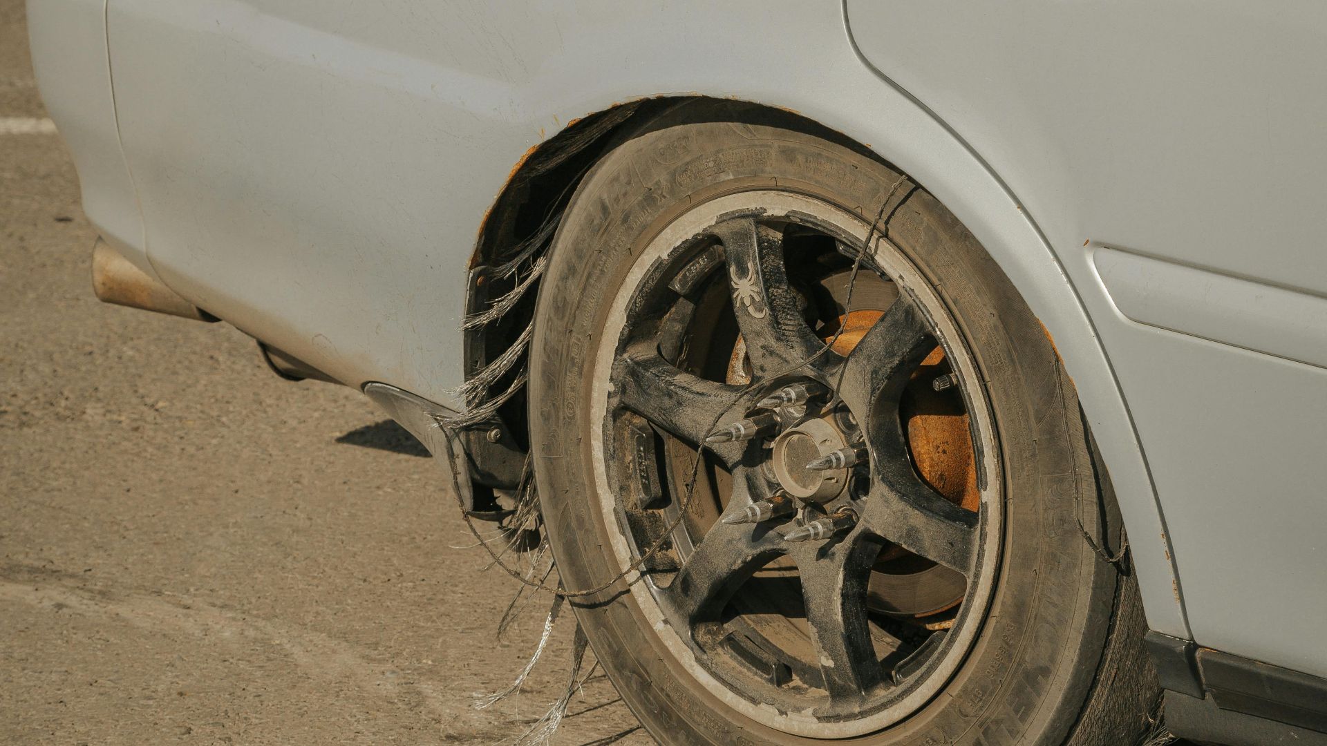 Close-up of a blue car with a severely damaged tire on weathered concrete.