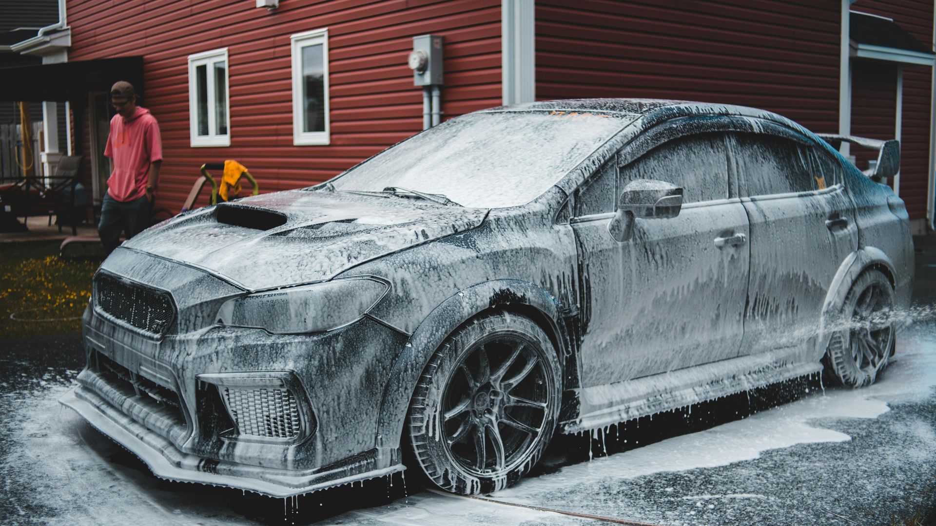 Unrecognizable African American worker standing by luxury sports car covered with foam at car wash in daytime