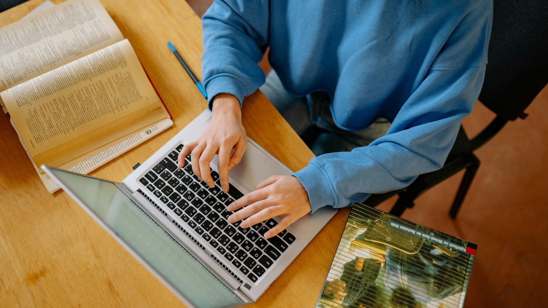 A student typing on a laptop surrounded by open books, focusing on research and school work.