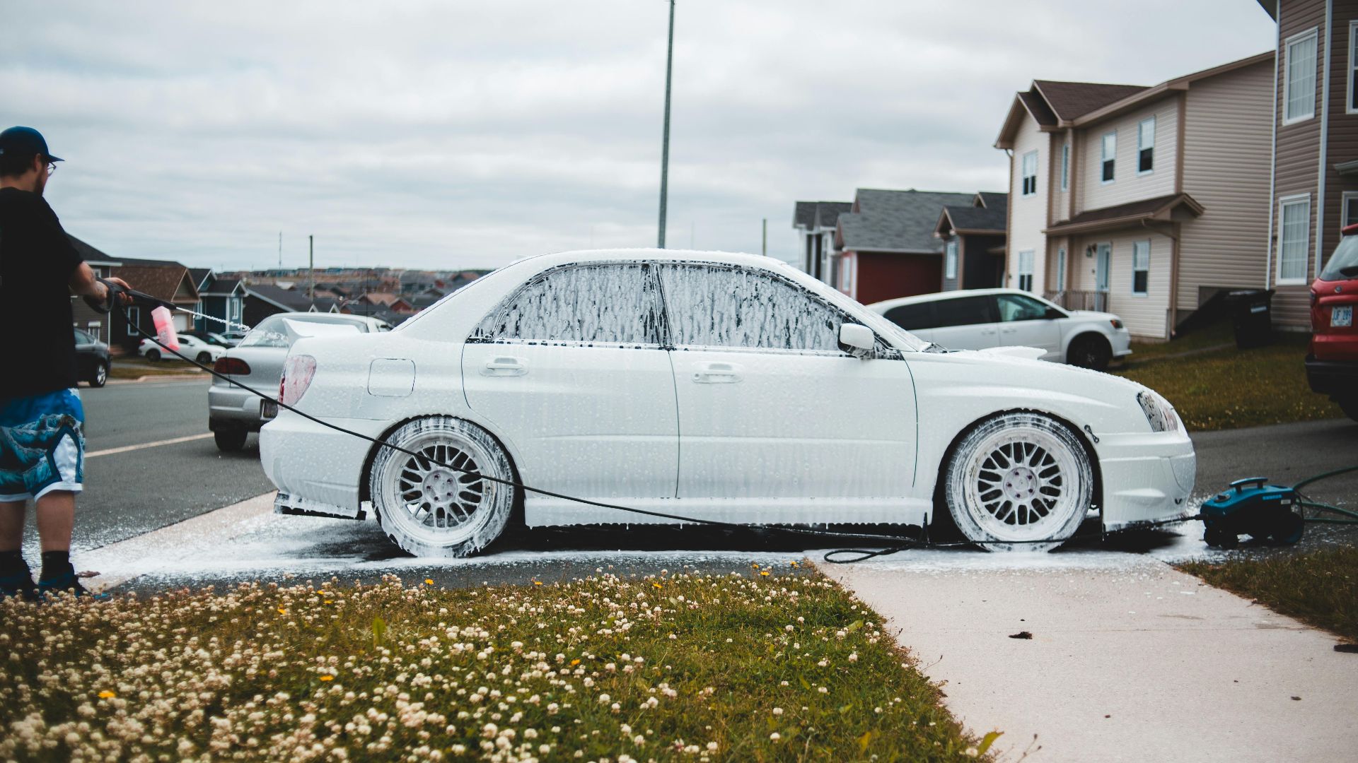 Foamed car on driveway and sidewalk being washed by male driver at daytime